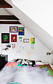 Bedroom with sloping ceiling, double bed with bedspread, retro bedside lamp and children's drawings