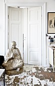 Large Buddha statue on floor with peeling paint in front of white double doors