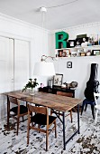 Rustic table and 60s-style wooden chairs below contemporary pendant lamp with white lampshade in dining room with distressed wooden floor