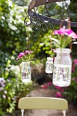 Flowers in glass bottles hanging on hooks in a garden