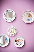 Colourful painted plates, some with mirrored centres, hung on lilac wall