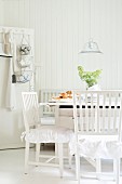 Scandinavian, white dining set with frilled cushions and tiered baskets suspended from peg on door in background