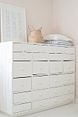 Cushions, rattan bag and picture on old, white-painted chest of drawers with shell handles