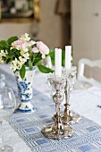 Silberne Kerzenleuchter und kleiner Blumenstrauss auf weiss-blau gemustertem Tischläufer