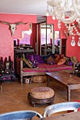 Eclectic style; comfortable living room with many cushions on wooden couch, mirror shaped like step pyramid, hunting trophy and pink wall