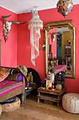 Pink living area with hunting trophy, decorative pendant lamp, altar with Buddha figurines and gilt-framed mirror