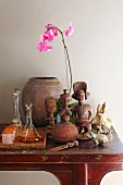 Folkloristische Figuren aus Holz neben Tablett mit Glaskaraffen und Becher, pinkfarbene Orchidee, auf Wandtisch