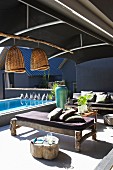 Rustic wooden benches with seat cushions on sunny terrace with dark fabric awning and pool in background