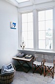 30s folding chair and folding table below lattice window; wicker basket of magazines on brick floor
