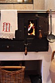 Wood-fired cooker with cloth and ladle hung from towel rail and view of fire through open firebox door