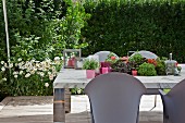 Hellgraue Outdoor Stühle um Tisch mit eingelassenem Blumenbehälter, im Hintergrund blühende Margeriten im Garten