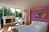 White sofa bed, set of coffee tables and open fireplace in living room with pink wall