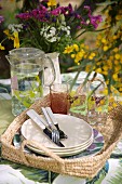 Glasses, jug of water and plates on basket tray outdoors