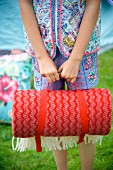 Rolled, red picnic blanket being held by girl in garden
