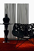 Plastic shell chair with perforated floral pattern and vase on pedestal tale on orange, long-pile rug