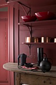 Various bowls on shelves and kitchen equipment on wooden table in Bordeaux red kitchen