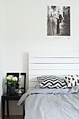 Black and white patterned scatter cushions on bed with white, wooden headboard next to black chair used as bedside table