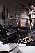Mysterious arrangement in archaic natural style - black leather armchair with knobbly wooden frame on shaggy rug and rope-style pendant lamps