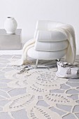 Elegant, feminine ambiance; white armchair on white rug with lace pattern, white vase on low, cubic coffee table in background