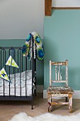 Wooden chair with peeling paint and cot with dark frame, bunting and crocheted blanket