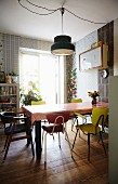 Colourful retro chairs at dining table with tablecloth below pendant lamp