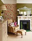 Armchair with footstool against floral wallpaper and open fireplace with shelves integrated into surround in traditional living room