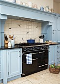 Vintage, black gas cooker under mantel hood flanked by country-house-style kitchen cabinets painted pale blue