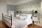 Double bed with black metal lattice frame against accent wall with floral wallpaper