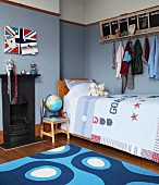 In blau getöntes Jungenzimmer mit Bett, Tafelboard mit Hakenleiste für Kleidung und Union Jack Flagge als Magnetbord