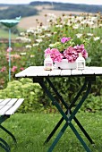 Pink hydrangeas in enamel bowl on folding garden table in front of bed of ox-eye daisies
