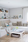 White, rustic coffee table in front of corner bench with seat cushions and scatter cushions in modern living room painted pale grey