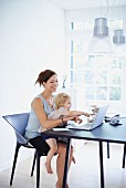Mother working on notebook with daughter on lap