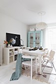White dining area with modern chairs around wooden table and pastel display cabinet in background