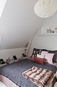 Double bed with blanket and arranged scatter cushions below sloping ceiling