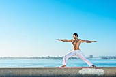 A young man by the sea wearing white yoga trousers