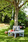 Shady seating area under tree with DIY tree bench painted pale grey and white