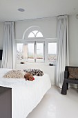 Fur scatter cushions on bed below window with semicircular fanlight in bedroom