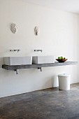 Concrete washstand with twin countertop basins below wooden masks on wall