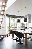 Upholstered swivel chairs at dining table below modern pendant lamps in open-plan kitchen with view of garden
