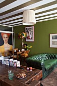 Green Chesterfield sofa, green accent wall and green and white striped ceiling in open-plan living are