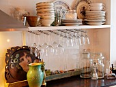 Wine glasses hung from racks below shelves of plates and bowls above kitchen counter