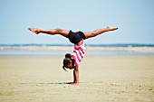 Sporty girl performing handstand on beach