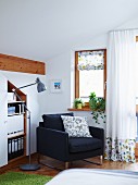 Einladender Lesesessel zwischen Einbauelement und Schlafzimmerfenster mit hellen Gardinen und Stoffrollo