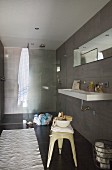 Designer bathroom in shades of grey with retro metal stool and shower area with glass screen
