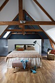 Double bed with bedspread against half-height partition screening ensuite bathroom in converted attic with exposed roof beams