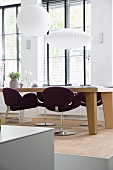 Purple swivel chairs at solid-wood dining table below white pendant lamps in front of lattice windows with louvre blinds