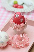 Red-dyed egg with floral motifs and pink trim in egg cup