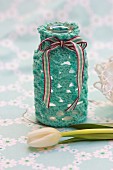 White tulip in front of bottle with hand-crocheted cover and ribbon