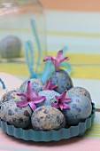 Dyed ornamental eggs and pink hyacinth florets in light blue, metal quiche tin