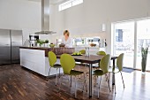 Dining table, green retro chairs and counter in elegant, open-plan kitchen with walnut parquet floor